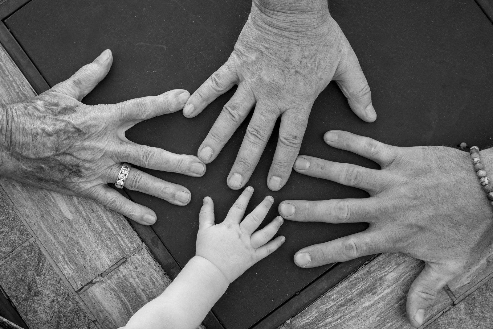 Hands of three generations of a family reaching toward each other